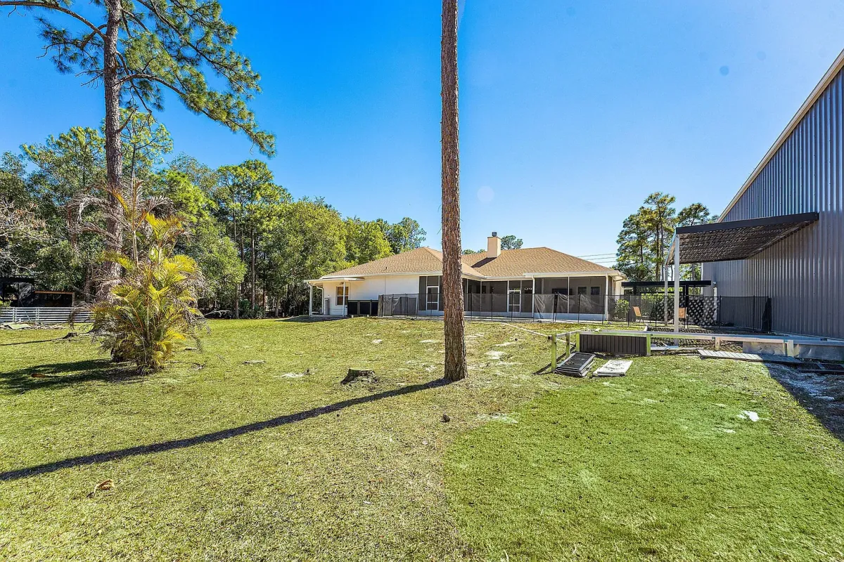 View across the 1.34-acre lot showing the house, the pool enclosure and the steel building