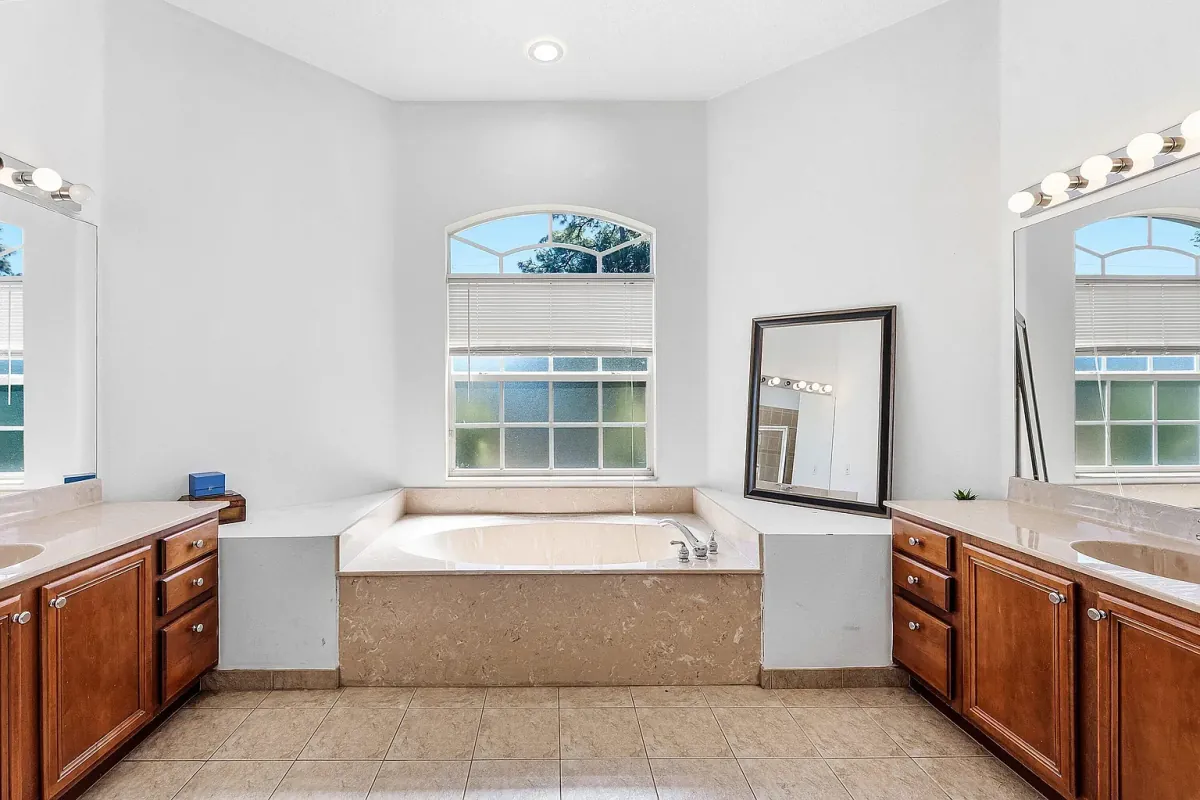 Primary bathroom with soaking tub set beneath an arched window and dual vanities