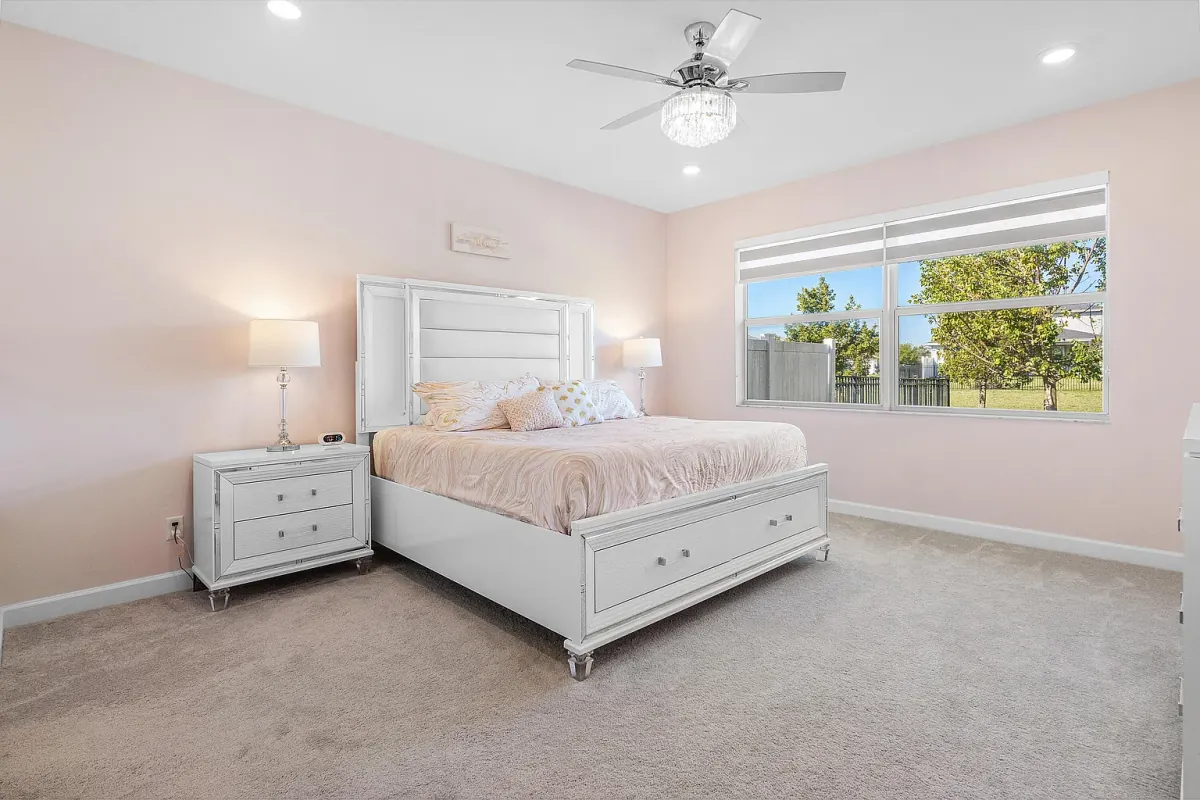Primary bedroom with ceiling fan and windows overlooking green space